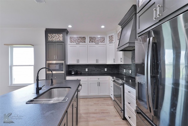 kitchen with light hardwood / wood-style flooring, appliances with stainless steel finishes, white cabinets, backsplash, and custom range hood