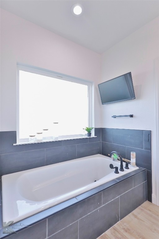 bathroom with tiled tub and wood-type flooring