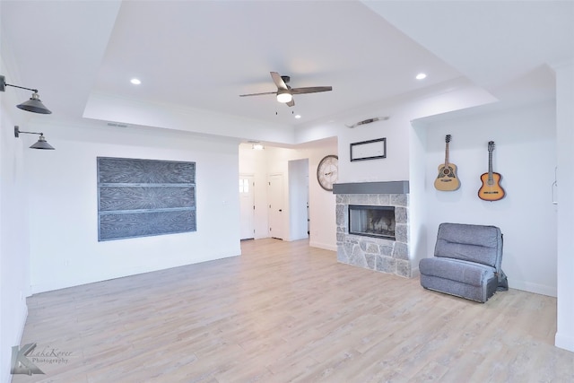 unfurnished living room featuring ceiling fan, a tile fireplace, a raised ceiling, and light hardwood / wood-style flooring