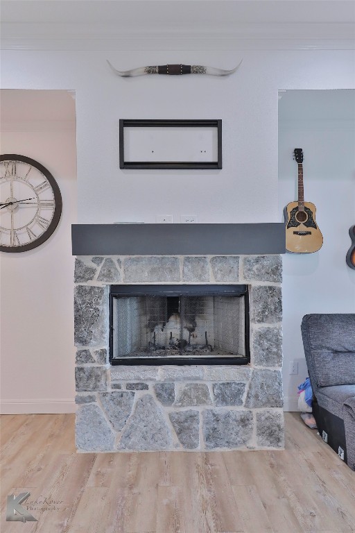 interior details featuring crown molding, a stone fireplace, and hardwood / wood-style flooring