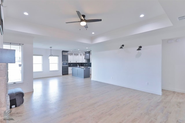 unfurnished living room with ceiling fan, a raised ceiling, light hardwood / wood-style flooring, and sink