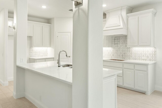 kitchen with tasteful backsplash, custom exhaust hood, black electric cooktop, white cabinets, and sink