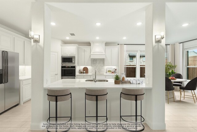 kitchen with white cabinetry, light wood-type flooring, custom range hood, appliances with stainless steel finishes, and tasteful backsplash