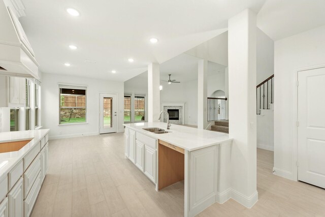 kitchen featuring light hardwood / wood-style floors, white cabinetry, a fireplace, a kitchen island with sink, and sink