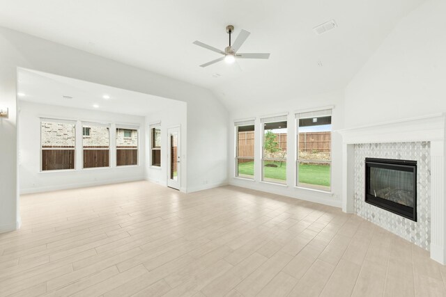 unfurnished living room featuring lofted ceiling, a tile fireplace, ceiling fan, and light hardwood / wood-style flooring