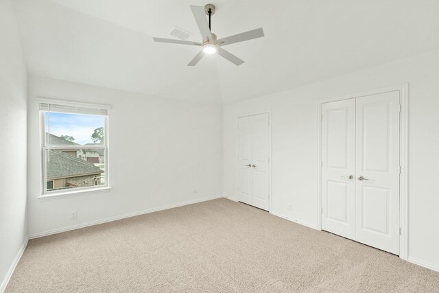 unfurnished bedroom featuring multiple closets, carpet, ceiling fan, and vaulted ceiling