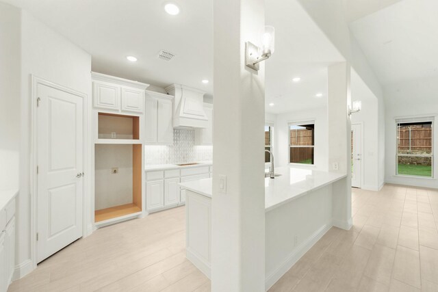 kitchen featuring custom range hood, backsplash, white cabinetry, sink, and stovetop