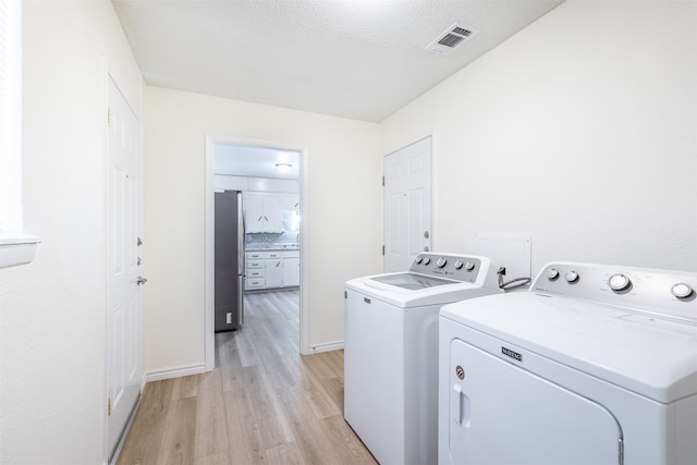 laundry area with light wood-type flooring, independent washer and dryer, and a textured ceiling