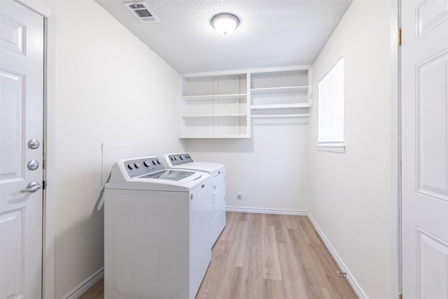 clothes washing area with washing machine and dryer, light wood-type flooring, and a textured ceiling