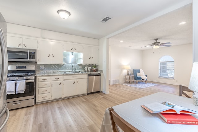 kitchen with light wood-type flooring, ceiling fan, stainless steel appliances, white cabinets, and tasteful backsplash