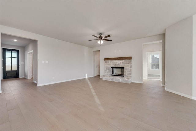 unfurnished living room featuring ceiling fan, a stone fireplace, light wood-type flooring, and a wealth of natural light