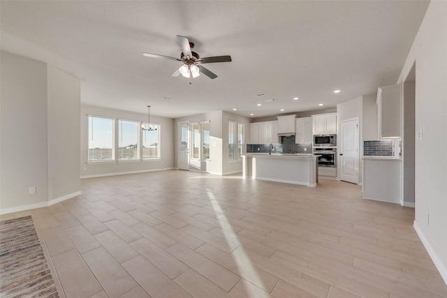 unfurnished living room with ceiling fan with notable chandelier and light hardwood / wood-style floors