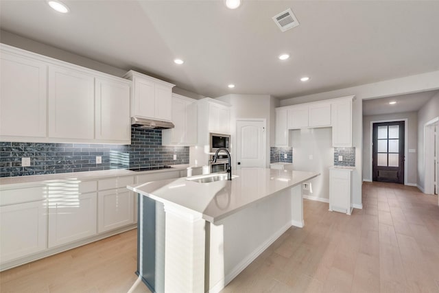 kitchen featuring extractor fan, sink, light hardwood / wood-style floors, white cabinetry, and an island with sink