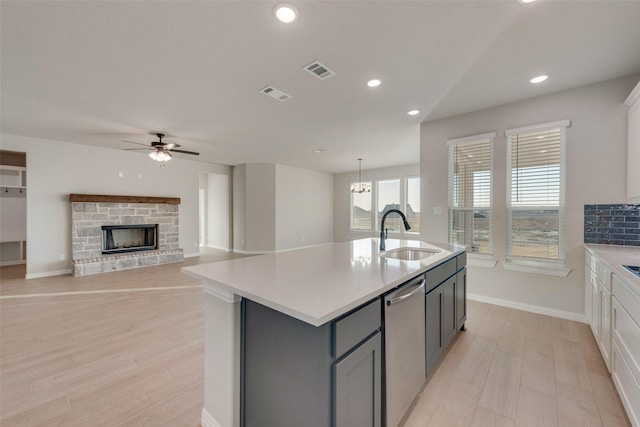 kitchen with sink, stainless steel dishwasher, a kitchen island with sink, ceiling fan with notable chandelier, and light wood-type flooring