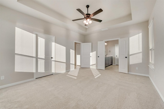 unfurnished bedroom featuring ensuite bathroom, ceiling fan, light colored carpet, and a tray ceiling