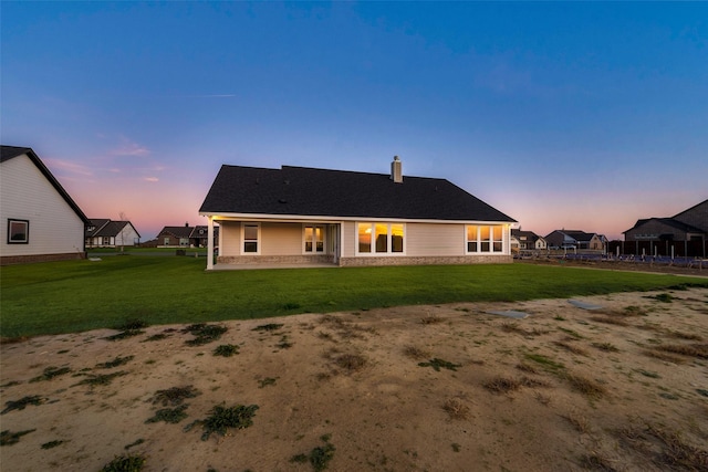 back house at dusk featuring a lawn