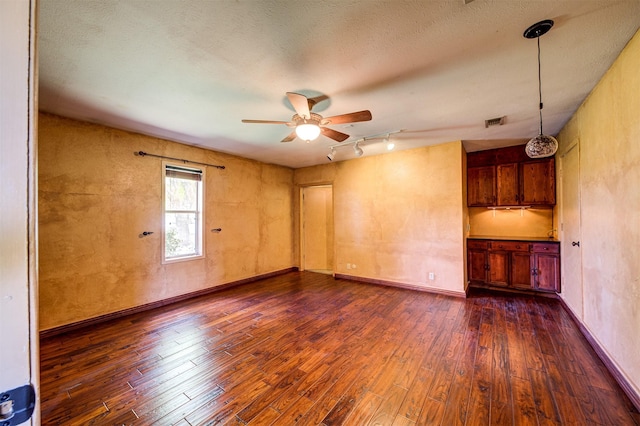 spare room featuring track lighting, dark wood-type flooring, visible vents, and a ceiling fan