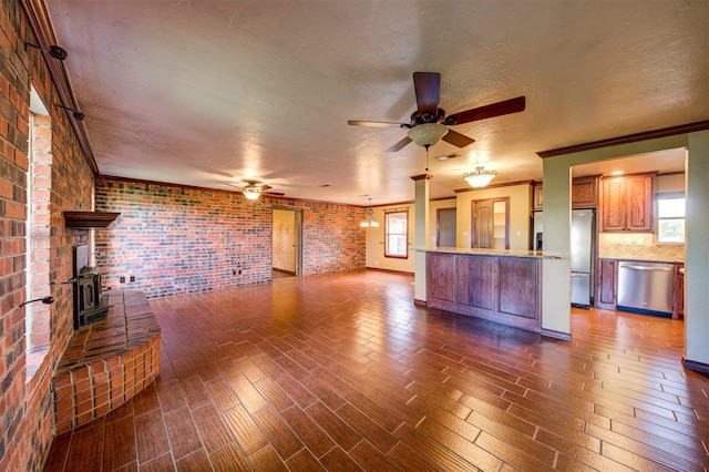 unfurnished living room with a wood stove, ceiling fan, brick wall, and plenty of natural light