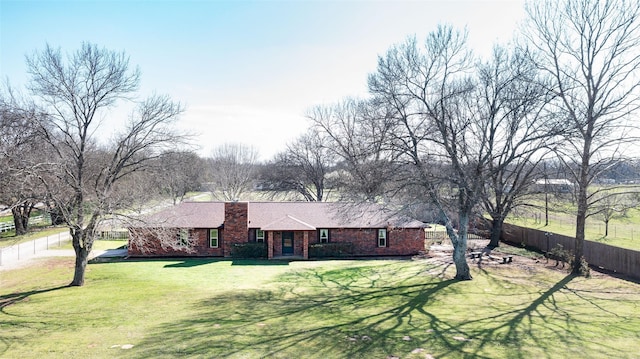 ranch-style home featuring a chimney, brick siding, fence, and a front lawn