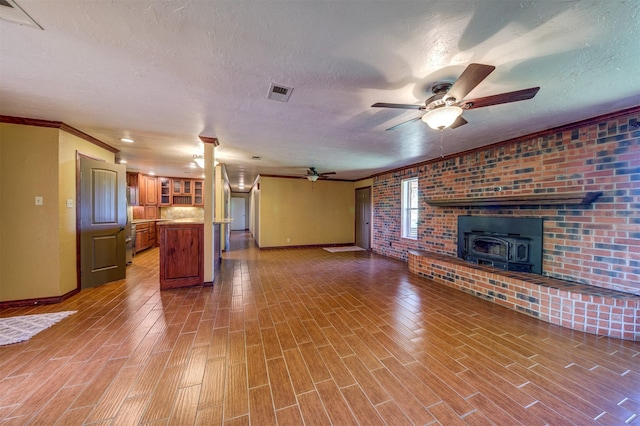 unfurnished living room with a wood stove, a ceiling fan, visible vents, and baseboards
