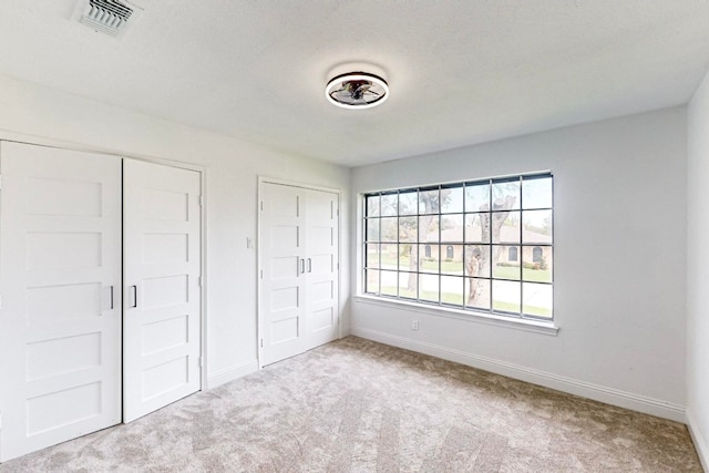 unfurnished bedroom with light colored carpet and multiple closets