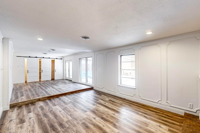 spare room featuring a barn door, a textured ceiling, and light hardwood / wood-style floors