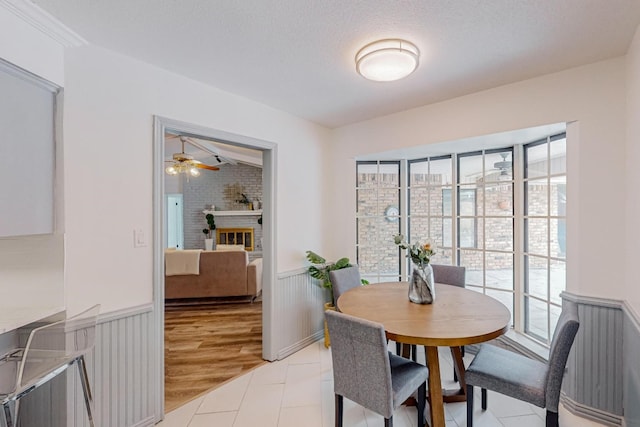 dining space featuring ceiling fan, a textured ceiling, light hardwood / wood-style flooring, and brick wall