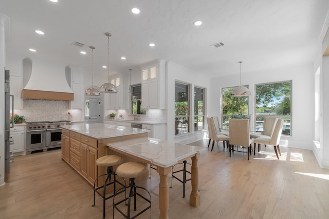 kitchen with a spacious island, custom exhaust hood, white cabinetry, and tasteful backsplash