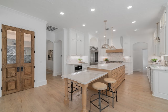 kitchen with appliances with stainless steel finishes, a spacious island, backsplash, white cabinetry, and light hardwood / wood-style flooring