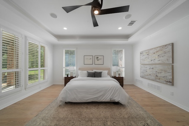 bedroom featuring light hardwood / wood-style floors, ornamental molding, a tray ceiling, and ceiling fan