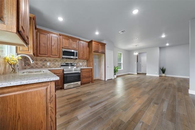 kitchen with decorative backsplash, stainless steel appliances, sink, hardwood / wood-style floors, and light stone counters