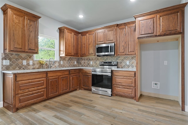 kitchen featuring light stone countertops, appliances with stainless steel finishes, sink, light wood-type flooring, and backsplash