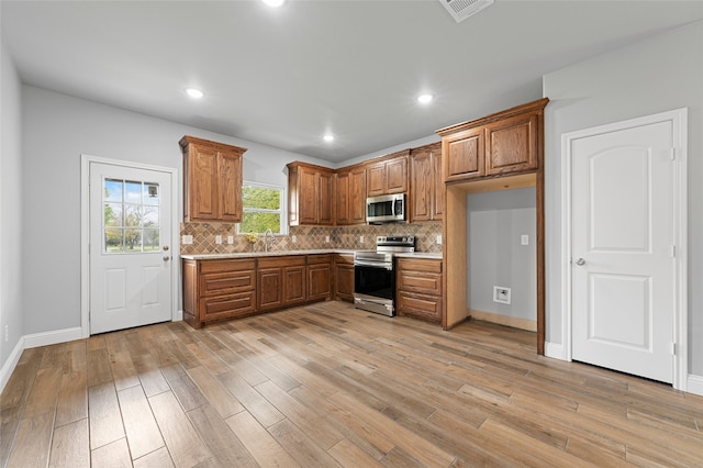 kitchen with appliances with stainless steel finishes, tasteful backsplash, sink, and light hardwood / wood-style floors