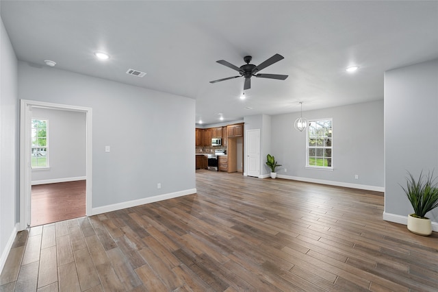 unfurnished living room with ceiling fan with notable chandelier and dark hardwood / wood-style flooring