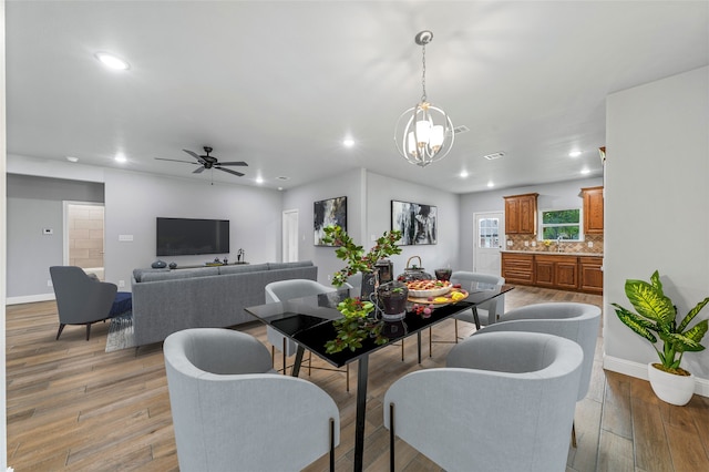 dining space with light hardwood / wood-style floors, sink, and ceiling fan with notable chandelier