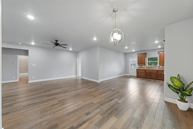 unfurnished living room featuring sink, wood-type flooring, and ceiling fan with notable chandelier