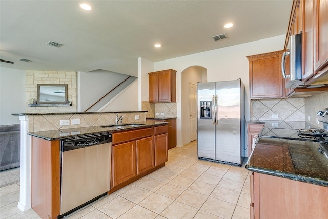 kitchen featuring appliances with stainless steel finishes, dark stone counters, backsplash, light tile floors, and sink