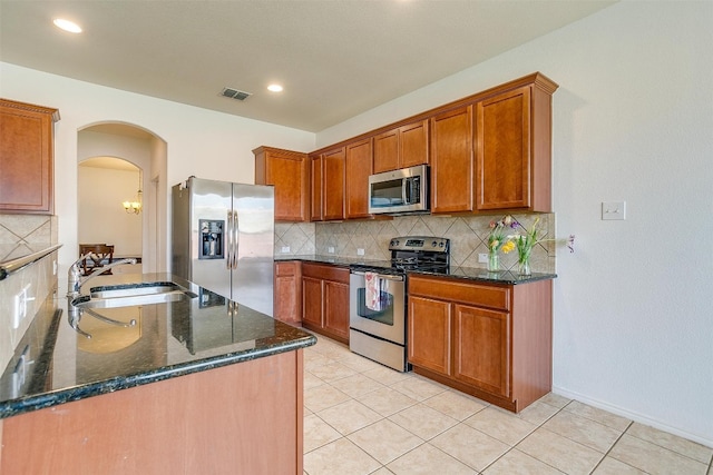 kitchen featuring appliances with stainless steel finishes, tasteful backsplash, dark stone countertops, sink, and light tile flooring