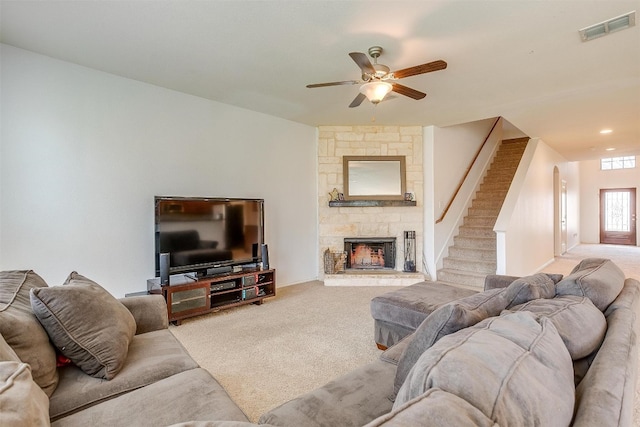 living room with ceiling fan, light colored carpet, and a stone fireplace