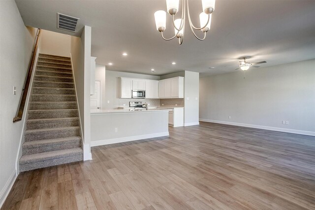 unfurnished living room with sink, ceiling fan with notable chandelier, and light hardwood / wood-style flooring