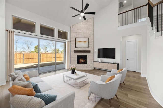 living room featuring ceiling fan, a fireplace, high vaulted ceiling, and light wood-type flooring