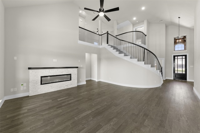 unfurnished living room featuring a fireplace, a towering ceiling, dark wood-type flooring, and ceiling fan with notable chandelier