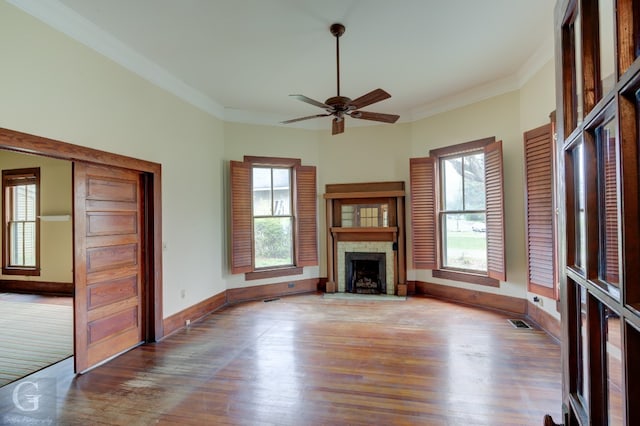 unfurnished living room with a stone fireplace, ceiling fan, dark hardwood / wood-style floors, and crown molding