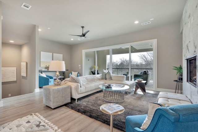 living room featuring ceiling fan, light hardwood / wood-style flooring, and a fireplace