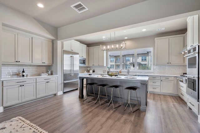 kitchen with a center island, backsplash, a kitchen bar, built in appliances, and light hardwood / wood-style flooring