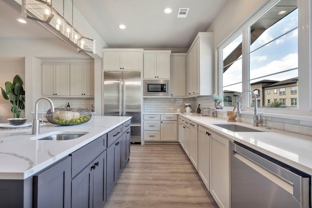 kitchen with pendant lighting, backsplash, light hardwood / wood-style floors, built in appliances, and white cabinets