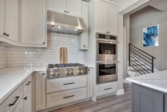 kitchen featuring light hardwood / wood-style floors, stainless steel appliances, white cabinetry, backsplash, and light stone counters