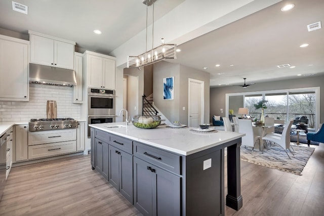 kitchen with decorative light fixtures, white cabinetry, light wood-type flooring, and stainless steel appliances