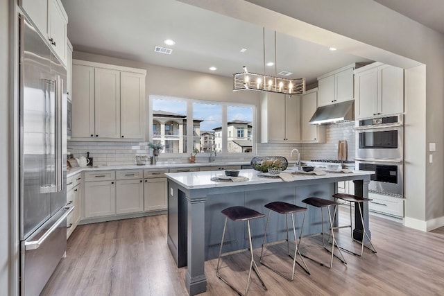 kitchen featuring decorative light fixtures, a kitchen bar, appliances with stainless steel finishes, light hardwood / wood-style floors, and a center island with sink