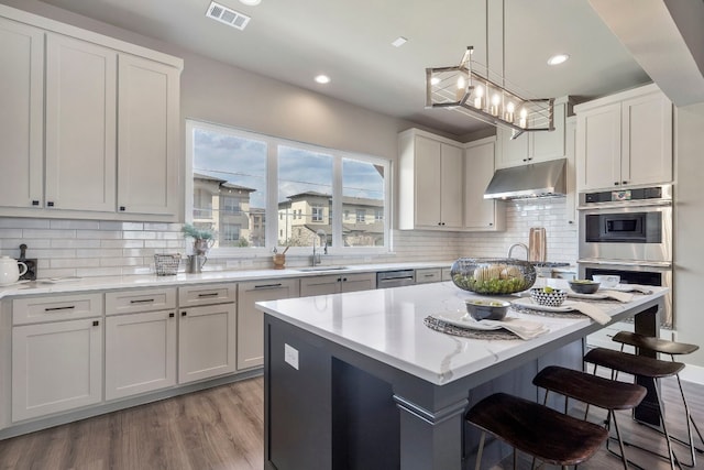 kitchen featuring hanging light fixtures, a center island, wood-type flooring, stainless steel appliances, and white cabinetry